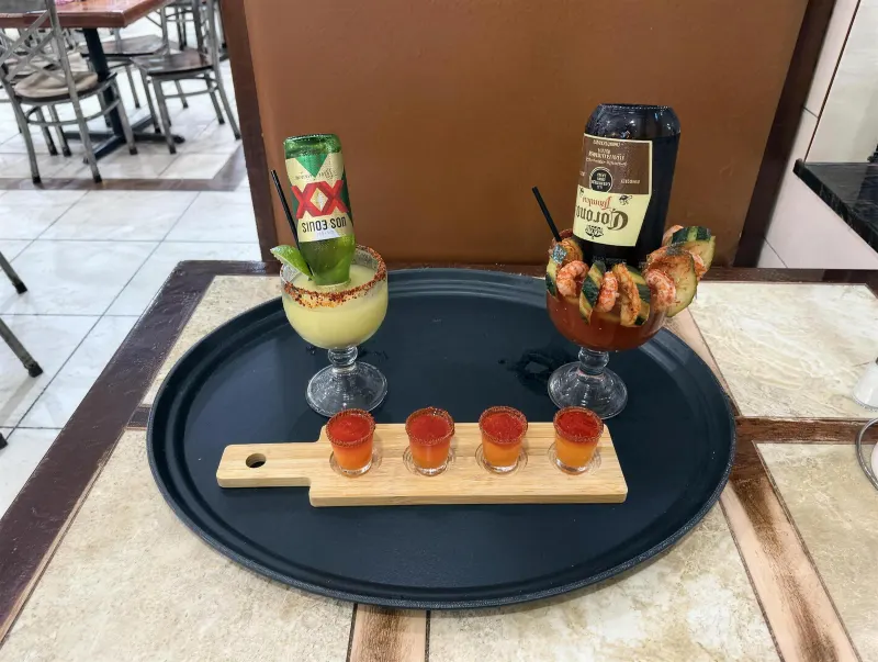The same three drinks — Beerita, shot flight and michelada — arranged on a black serving tray