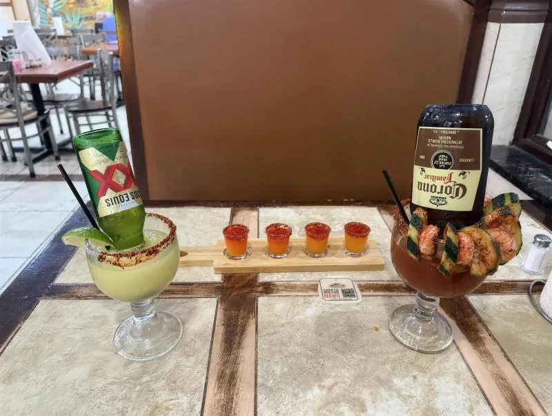 A Beerita with an inverted Dos Equis bottle, the shot flight and a shrimp-and-cucumber michelada set out on a tiled table