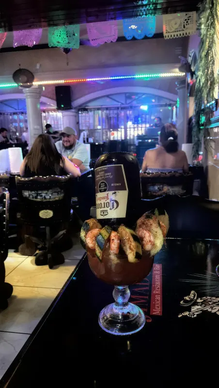 A second view of the michelada on the table, guests seated in the studded barrel chairs under the colored string lights and papel picado